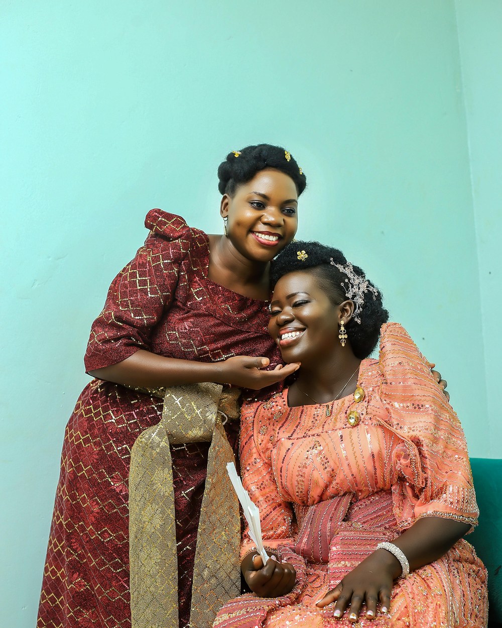Two women wearing gomesi in contrasting peach and maroon fabrics