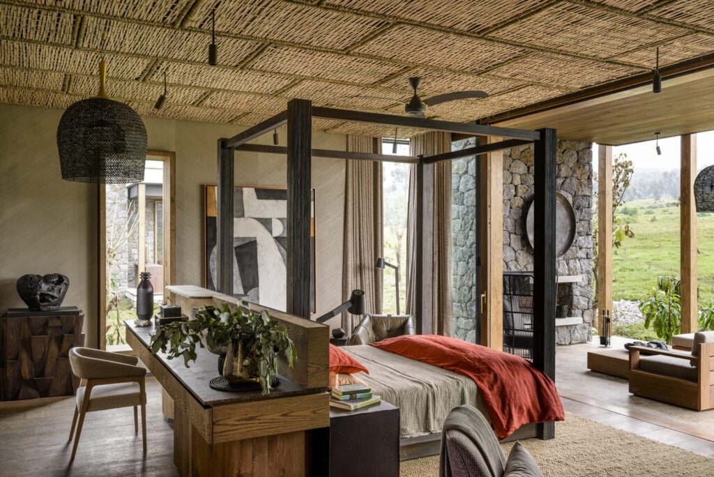 A one-bedroom suite at Singita Kwitonda Lodge with a dark timber four-poster bed, woven ceiling and doors opening onto the landscape