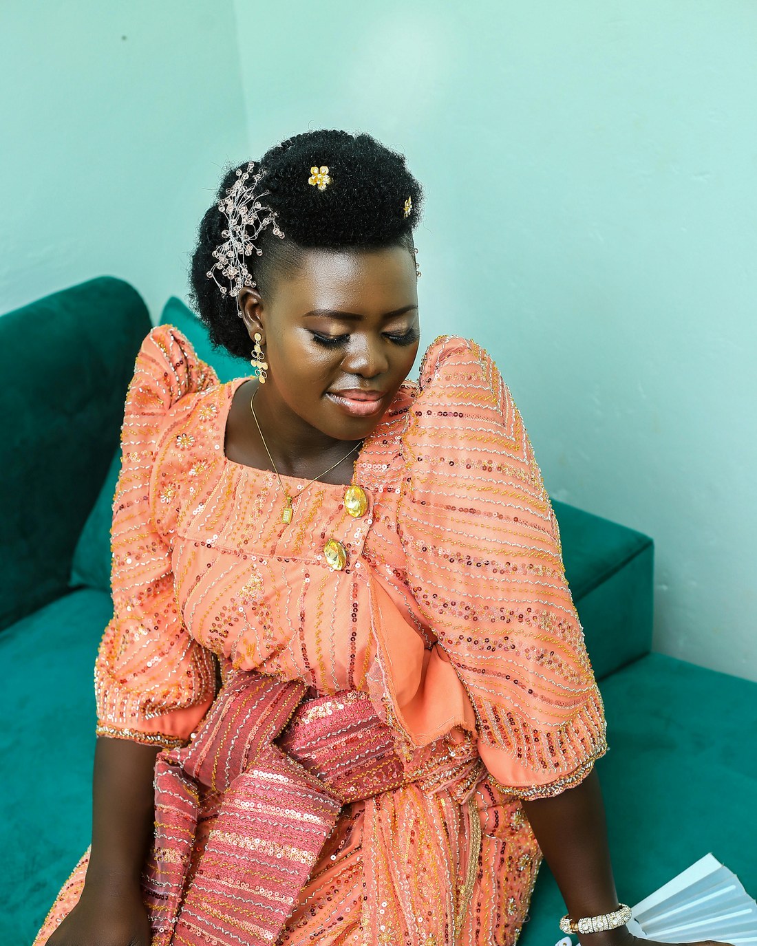 Woman seated in a coral gomesi with the sash and structured shoulder visible